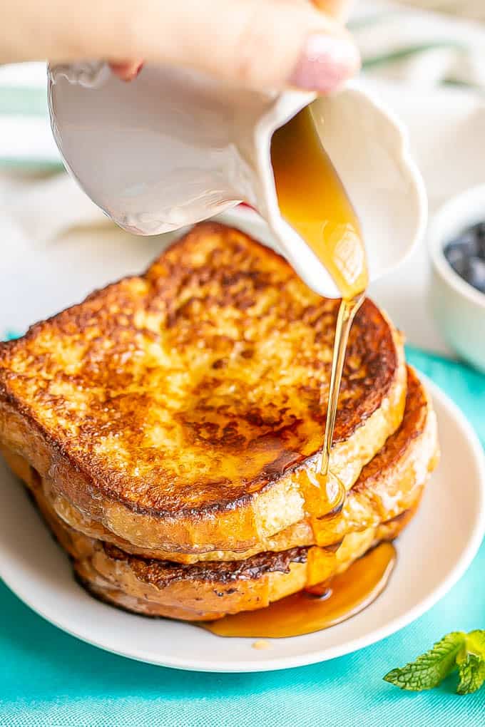 Maple syrup being poured over a stack of homemade easy French toast on a white plate