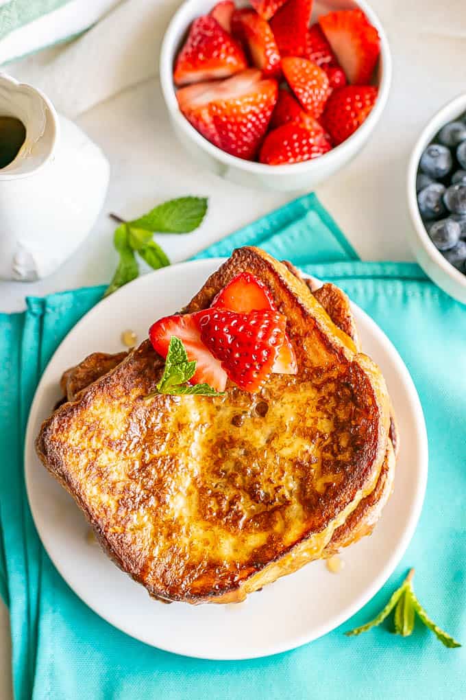 Overheat shot of cooked, browned French toast slices on a white plate with bowls of fresh berries nearby