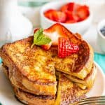 Stacked slices of French toast on a plate with berries on top and a small bite cut out with a text overlay on the image