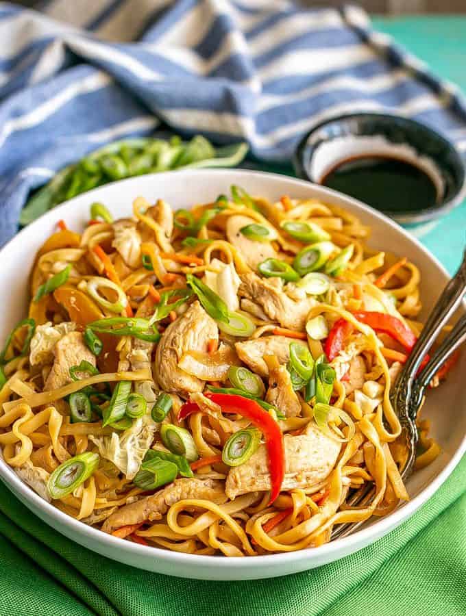 A shallow, wide white bowl full of chicken lo mein topped with sliced green onions