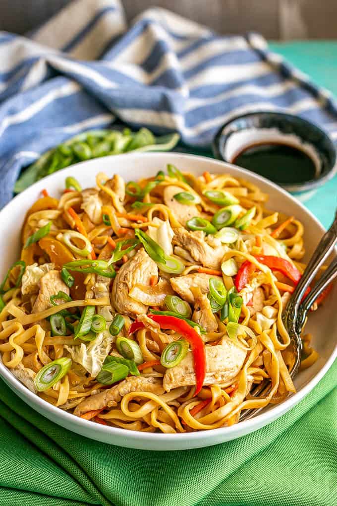 A shallow, wide white bowl full of chicken lo mein topped with sliced green onions