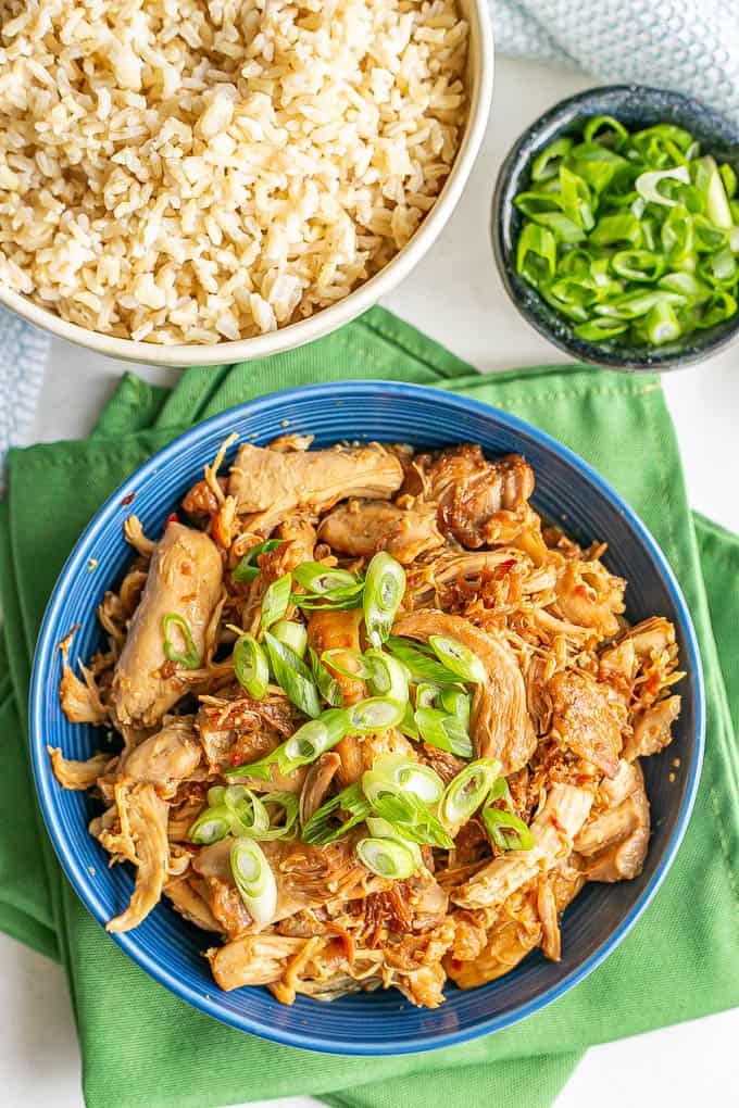 Pressure cooker honey garlic chicken served in a blue bowl with green onions on top and a bowl of rice to the side