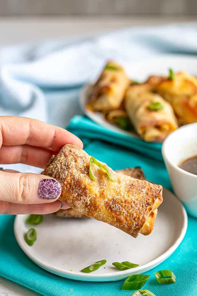 A hand picking up an Air Fryer vegetable egg roll from a small white plate