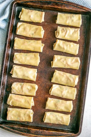 A baking sheet with wrapped egg rolls before being baked