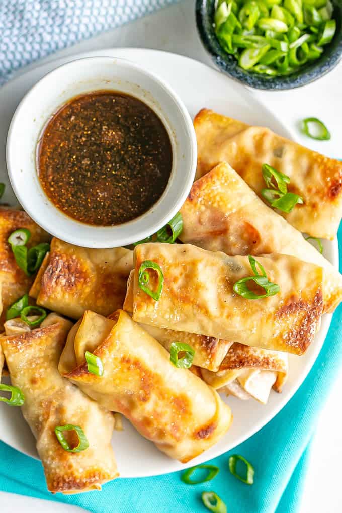 Close up of plate of stacked baked vegetable egg rolls sprinkled with sliced green onions with a small bowl of dipping sauce