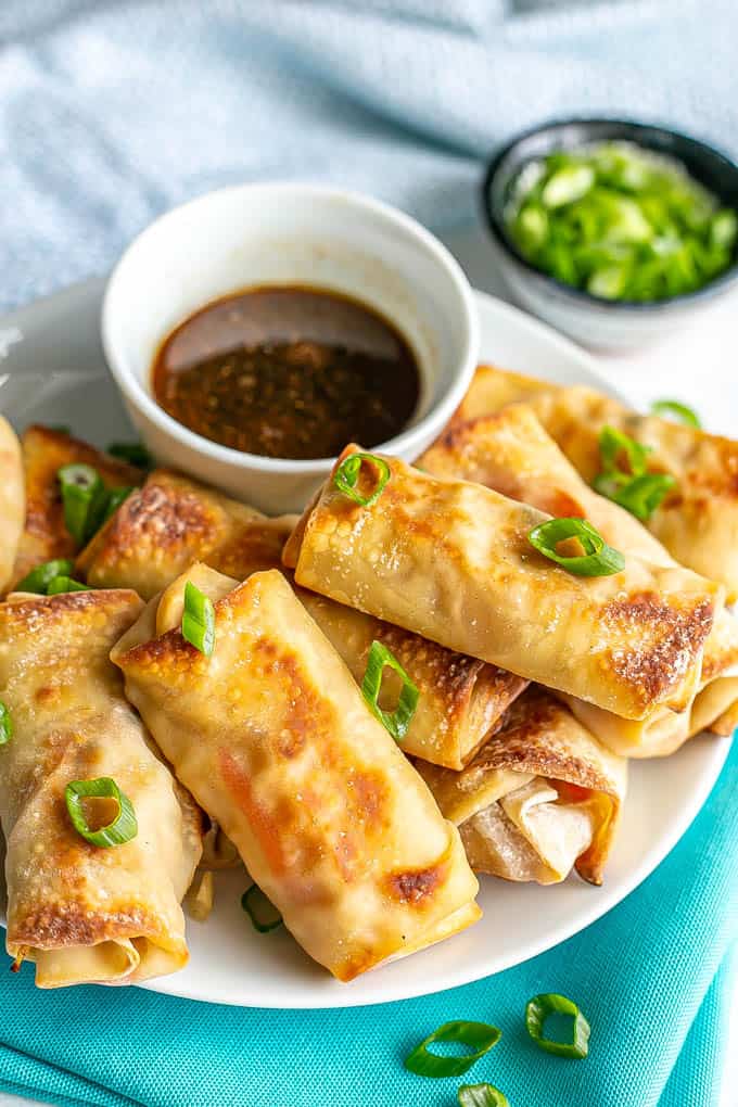 A plate of stacked baked vegetable egg rolls with a small bowl of dipping sauce