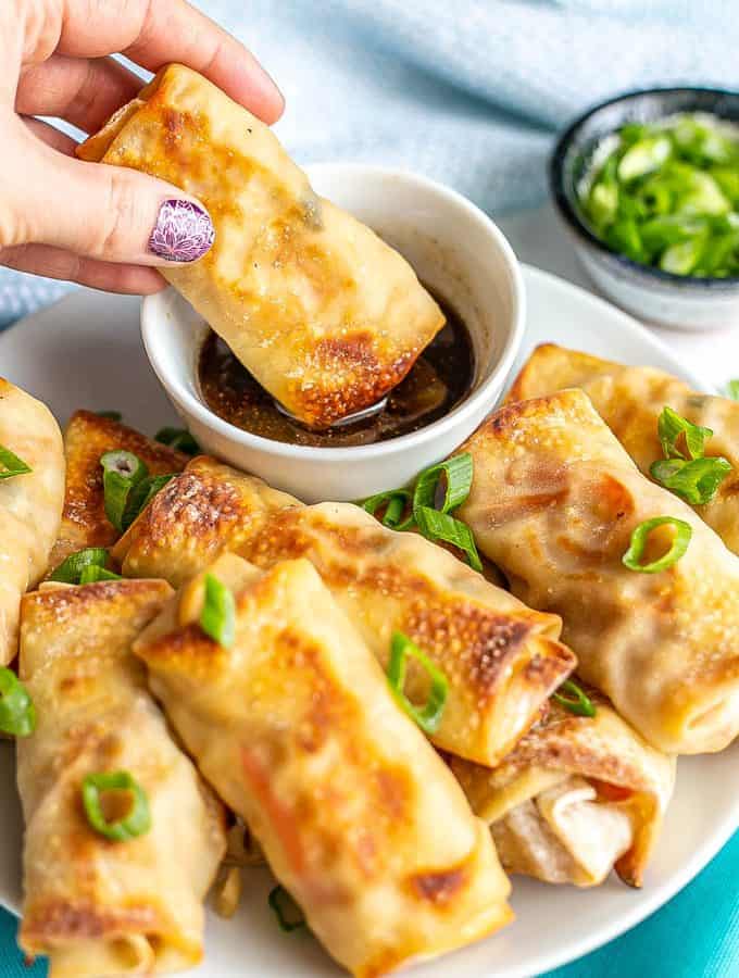 A hand dipping a baked vegetable egg roll into a soy sauce based dipping sauce