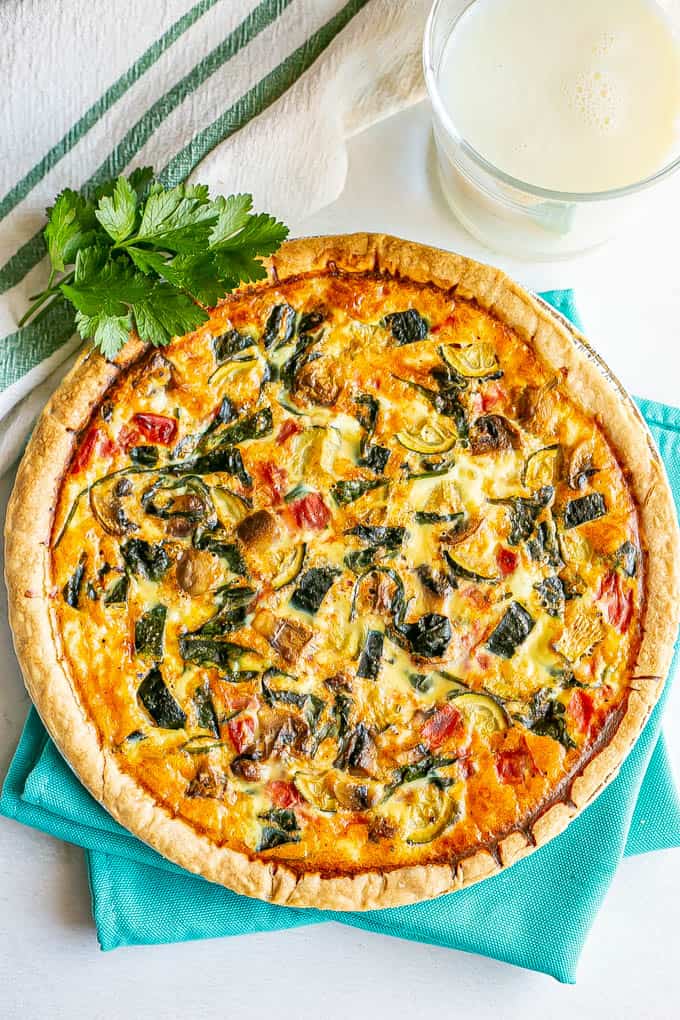 A baked golden brown veggie loaded quiche with sprigs of parsley for garnish and a glass of milk nearby