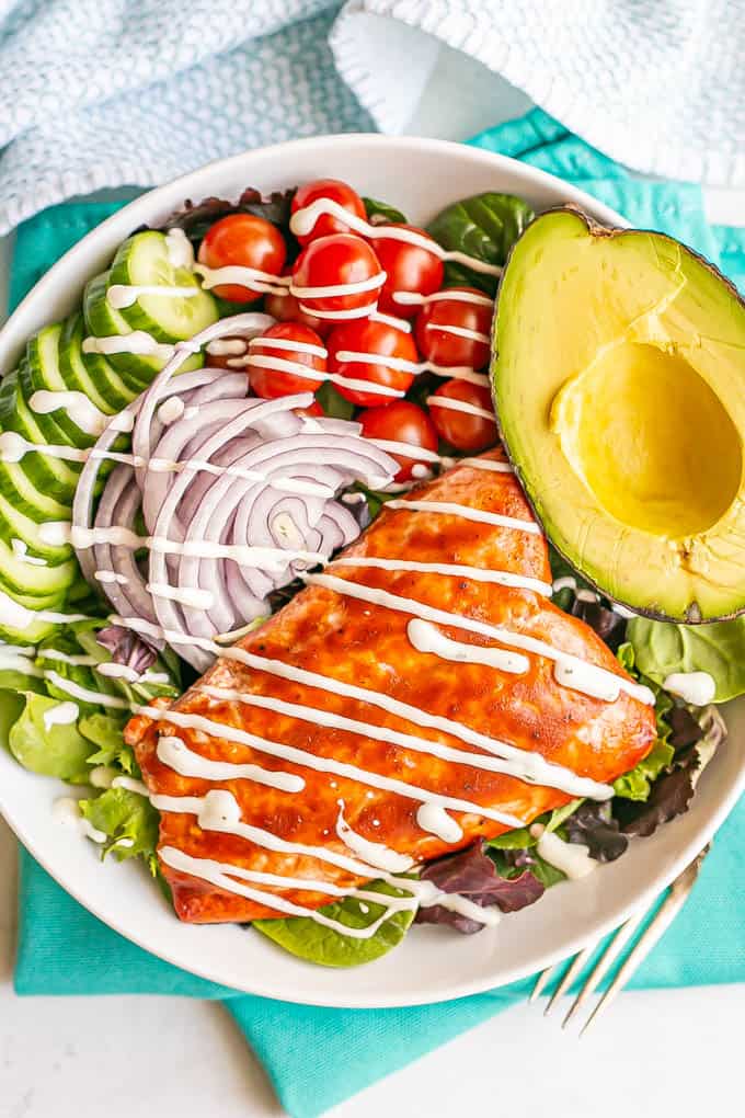 Mixed greens and veggie salad with BBQ salmon, avocado and a creamy dressing in a large white bowl