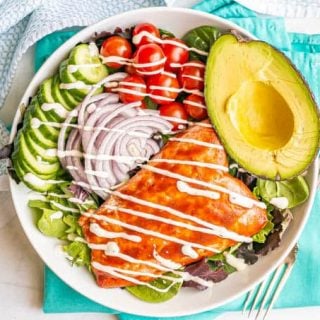 Overhead shot of a salad with cucumbers, tomatoes, red onion, avocado and a filet of BBQ salmon with a drizzle of dressing over everything