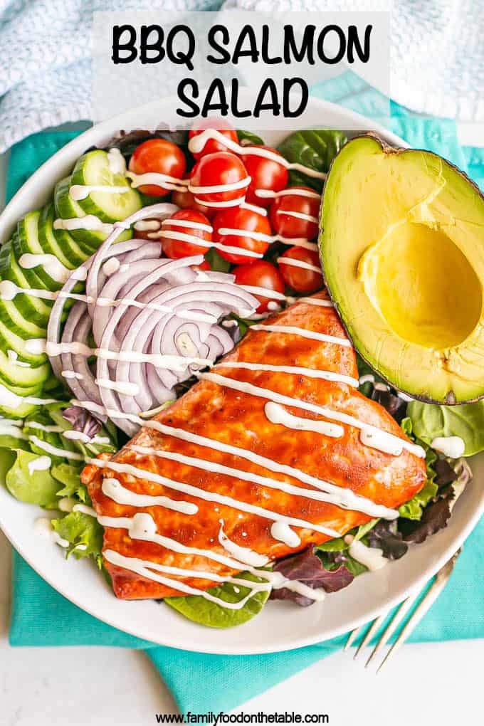 Mixed greens and veggie salad with BBQ salmon, avocado and a creamy dressing in a large white bowl with a text overlay on the photo