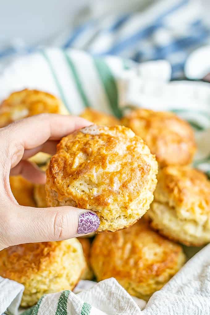 A hand picking up a butter-brushed biscuit from a basket of biscuits