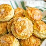 A napkin lined basket with fluffy, browned and buttery homemade biscuits with a text overlay on the photo