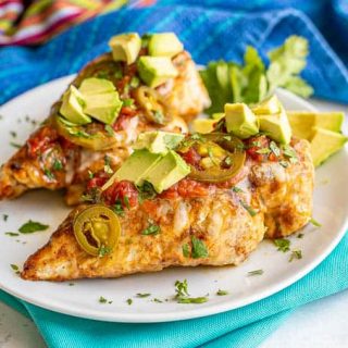Grilled chicken breasts served on a white plate set over turquoise napkins and topped with cheese, salsa, avocado, jalapeños and cilantro