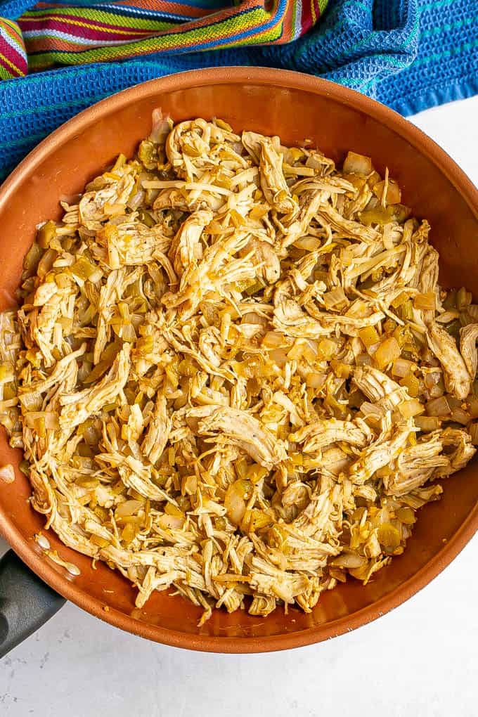 A large copper skillet with a shredded chicken and green chile mixture