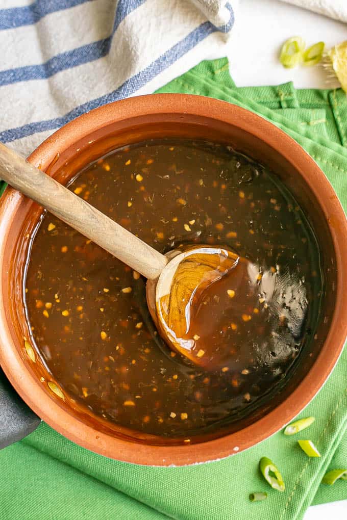 A wooden spoon resting in a small copper saucepan with cooked teriyaki sauce