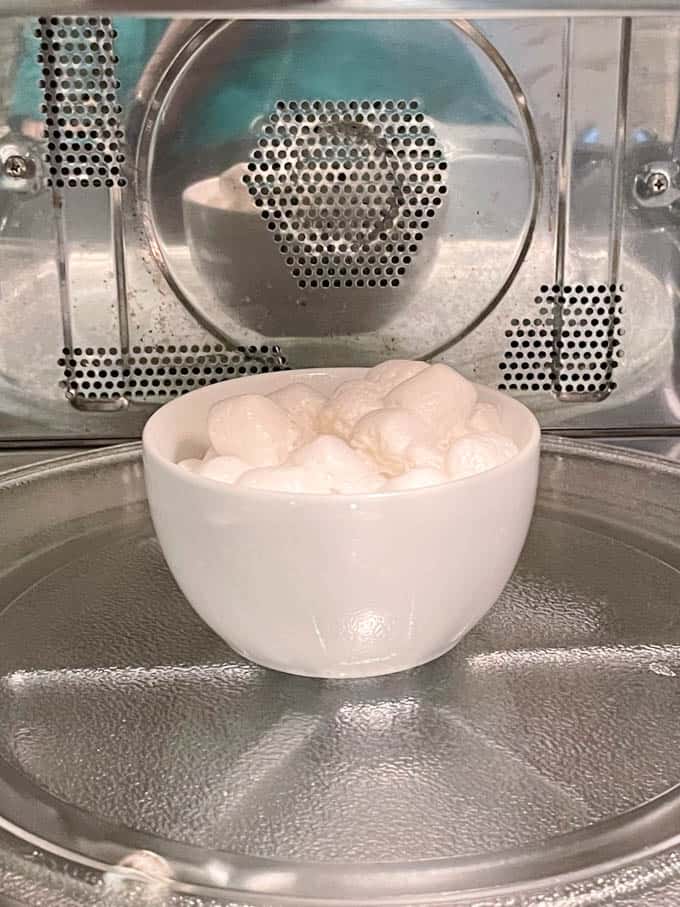 Marshmallows in a small white bowl in the microwave as they are being heated