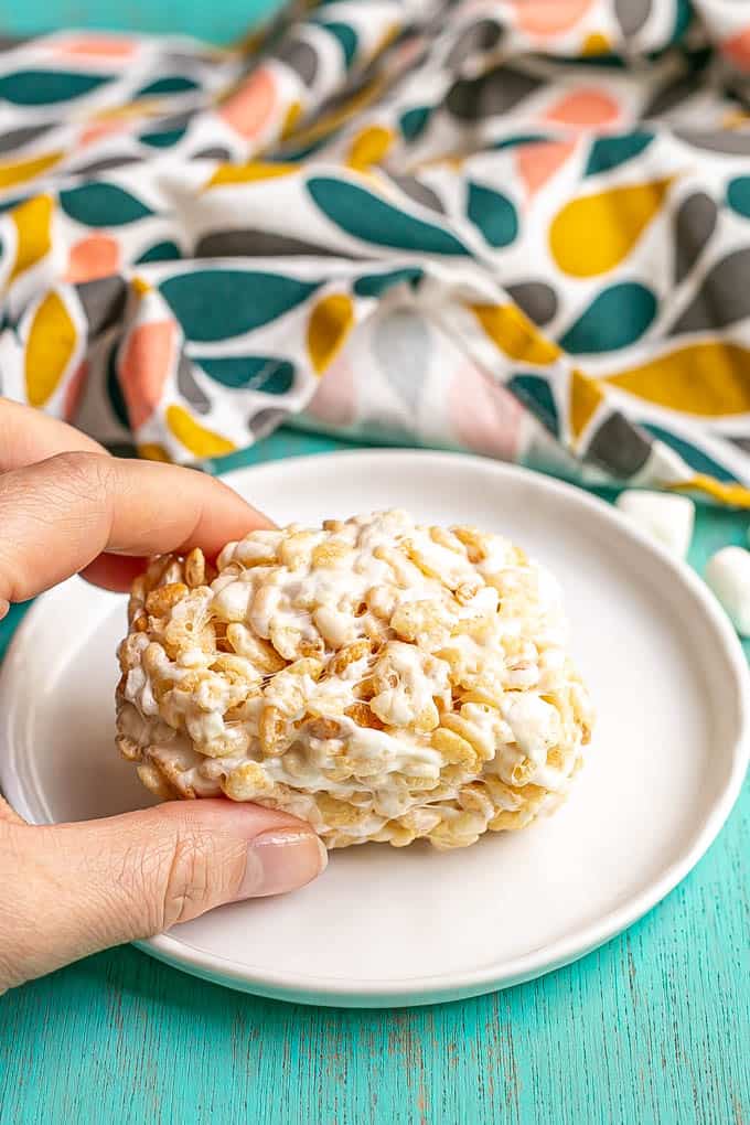 A hand picking up a Rice Krispie treat from a small white plate