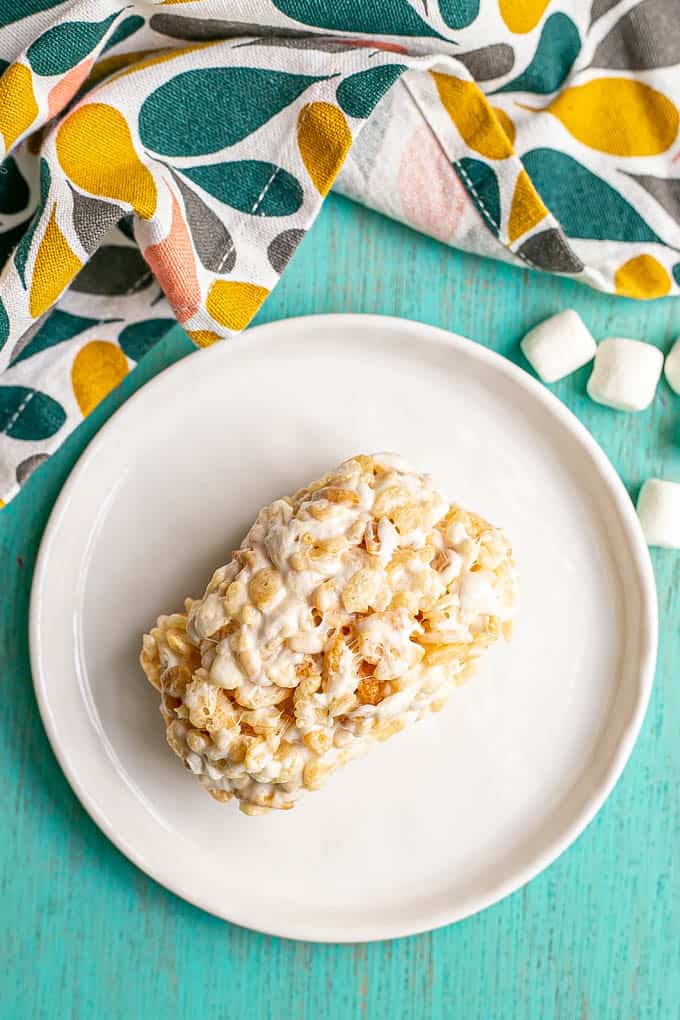 A single Rice Krispie treat on a small white plate with mini marshmallows scattered nearby