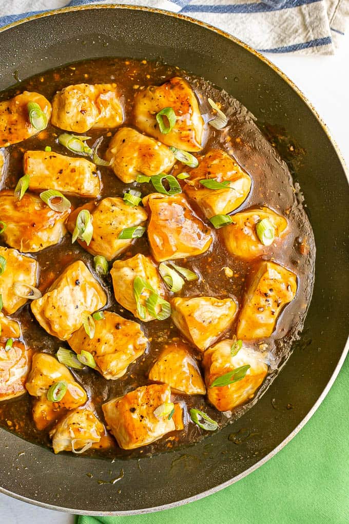 Close up of cubed chicken pieces in teriyaki sauce in a large skillet with sliced green onions on top