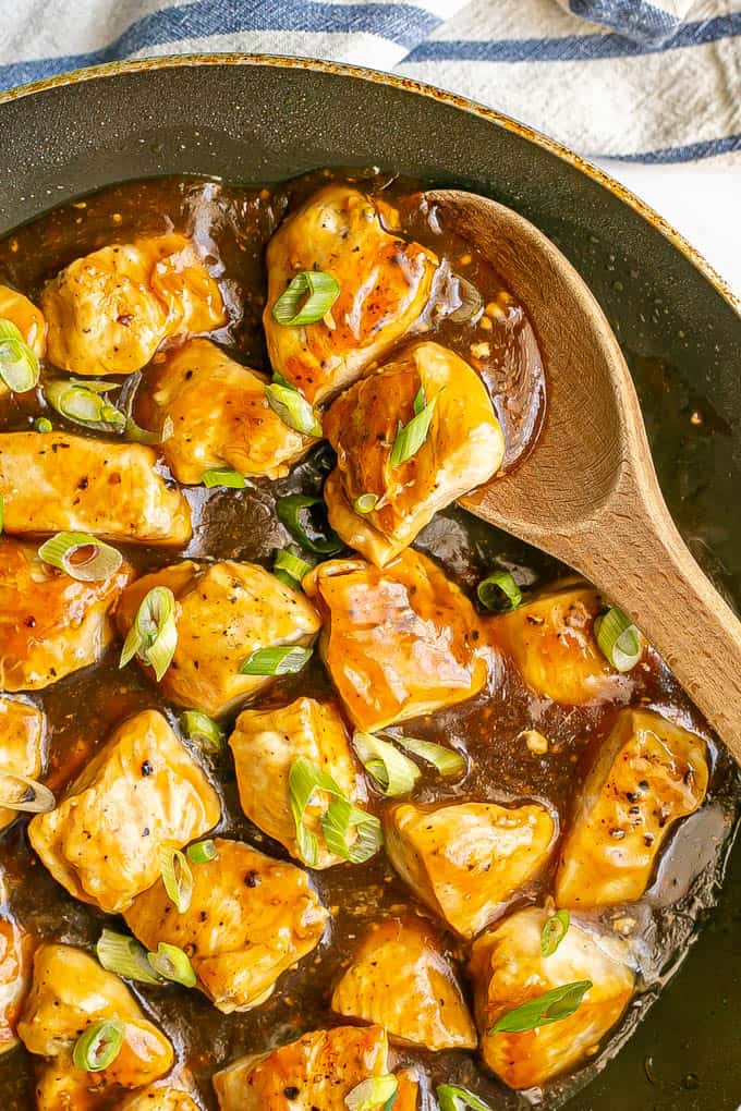 A wooden spoon resting in a large skillet with cooked cubed pieces of teriyaki chicken