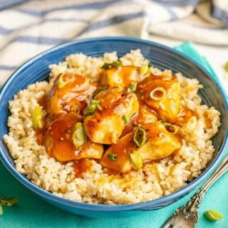A blue bowl with steamed brown rice topped with saucy teriyaki chicken and sliced green onions