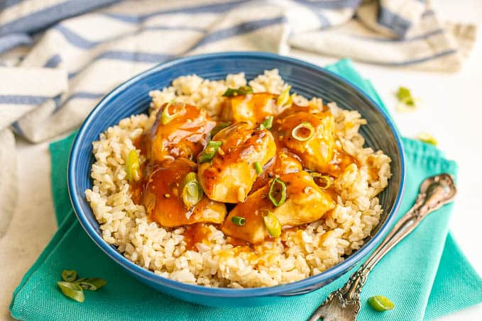 A blue bowl with steamed brown rice topped with saucy teriyaki chicken and sliced green onions