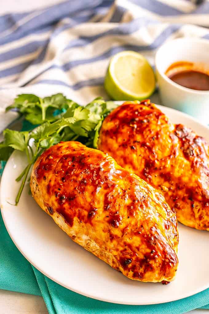 Grilled adobo chicken breasts on a white plate with parsley, lime and a small bowl of adobo sauce nearby