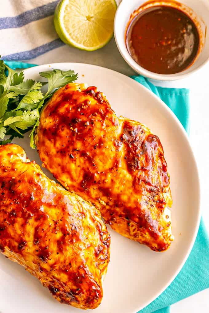 Grilled chicken breasts basted with adobo sauce and served on a white plate with parsley to the side