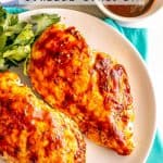 Grilled chicken breasts basted with adobo sauce and served on a white plate with parsley to the side and a text overlay on the photo