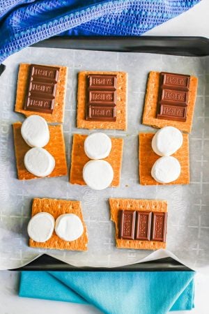 A tray of graham cracker sheets with chocolate and marshmallows on top before being baked in the oven to make s'mores