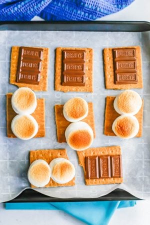 A tray of oven baked s'mores with toasted marshmallows and melty chocolate on graham cracker sheets