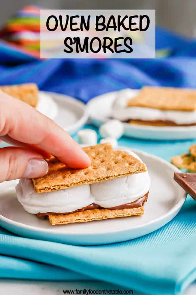 A hand smushing down a s'mores sandwich on a small white plate with a text overlay on the photo
