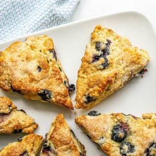 Overhead shot of a plate full of blueberry scones with fresh blueberries scattered nearby
