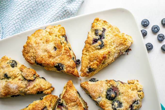 Overhead shot of a plate full of blueberry scones with fresh blueberries scattered nearby