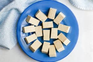 Uncooked tofu cut into cubes and arranged on a blue plate