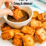 A hand dipping a crispy tofu piece into a soy sauce dipping sauce with a text overlay on the photo