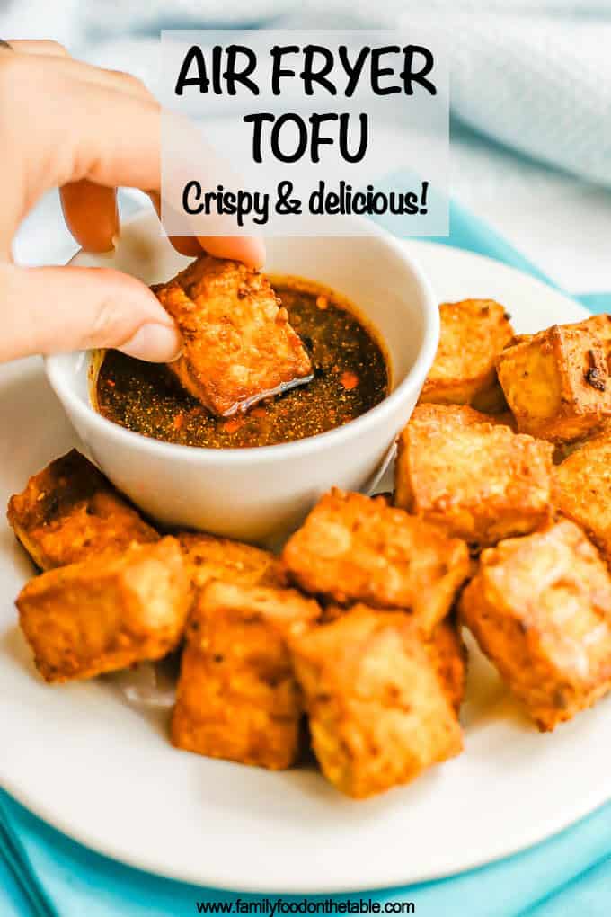 A hand dipping a crispy tofu piece into a soy sauce dipping sauce with a text overlay on the photo