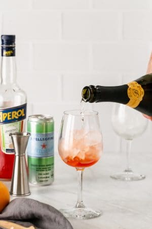 Sparkling wine being poured over ice and Aperol in a wine glass