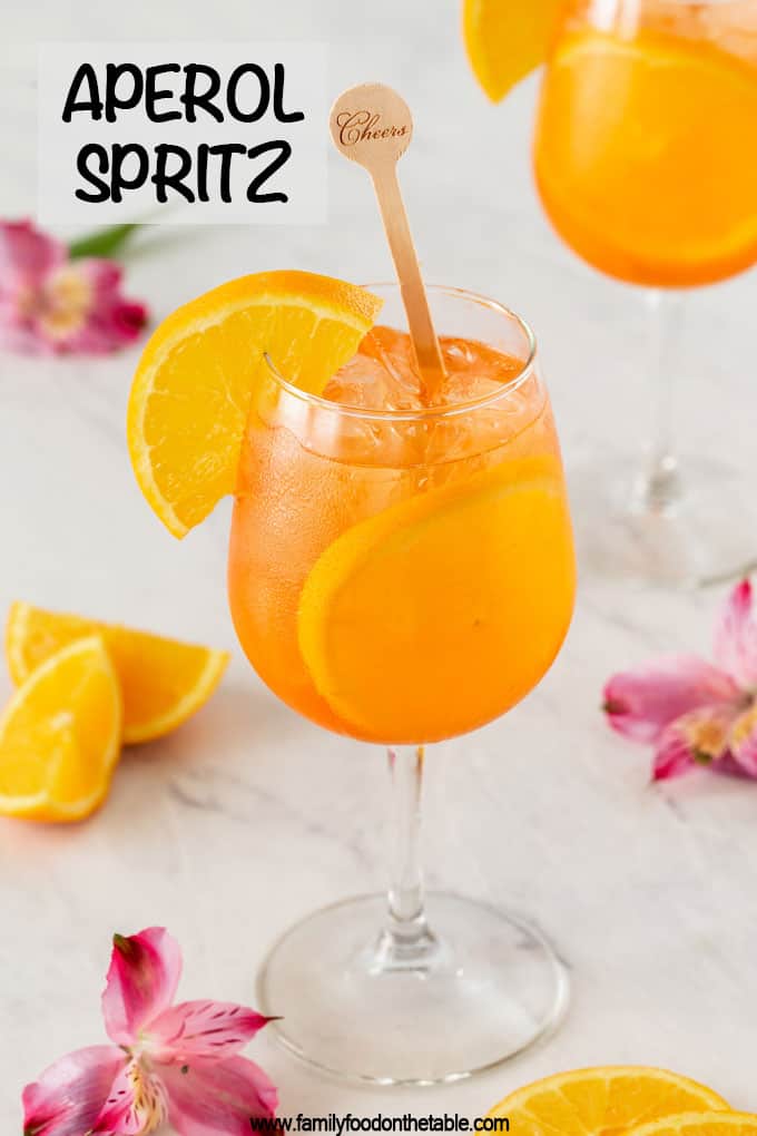 A wine glass with an Aperol Spritz cocktail and orange slices with a text overlay on the photo