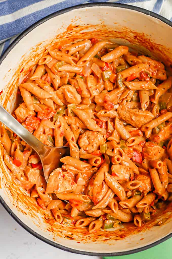 A large pot full of a creamy cajun chicken pasta with tomatoes and veggies, with a silver spoon dipped in