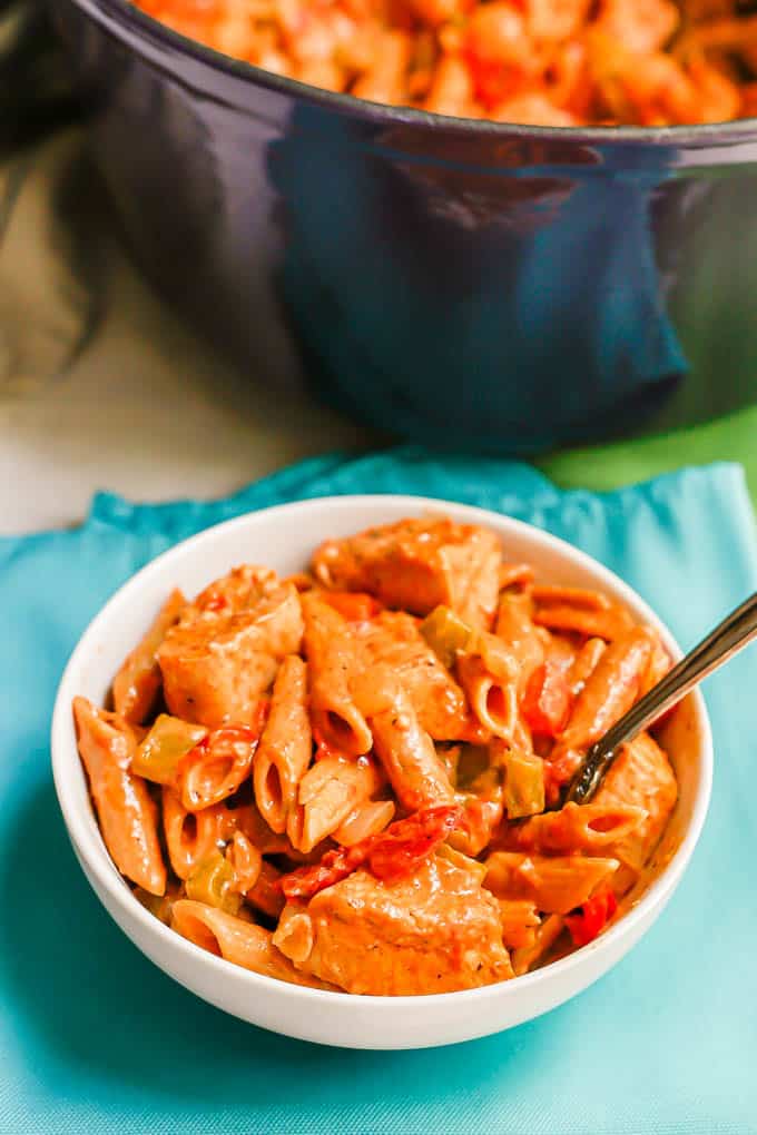 A white bowl with a serving of Cajun chicken pasta and a fork resting in the bowl