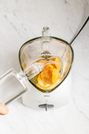 Overhead shot of a blender with orange juice concentrate in it and vodka being added
