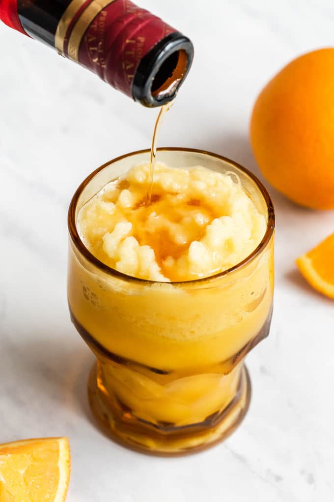 Orange liqueur being added to a frozen slushy orange drink in a glass