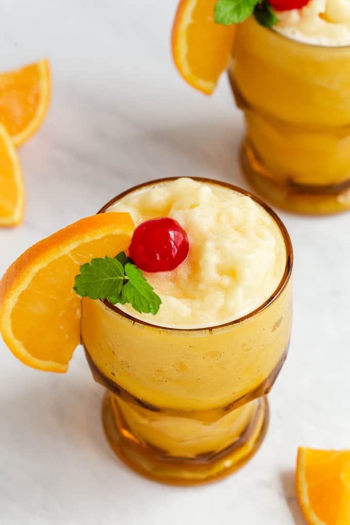 Close up of a frozen screwdriver in a short amber glass with an orange slice, cherry and mint sprig for garnish