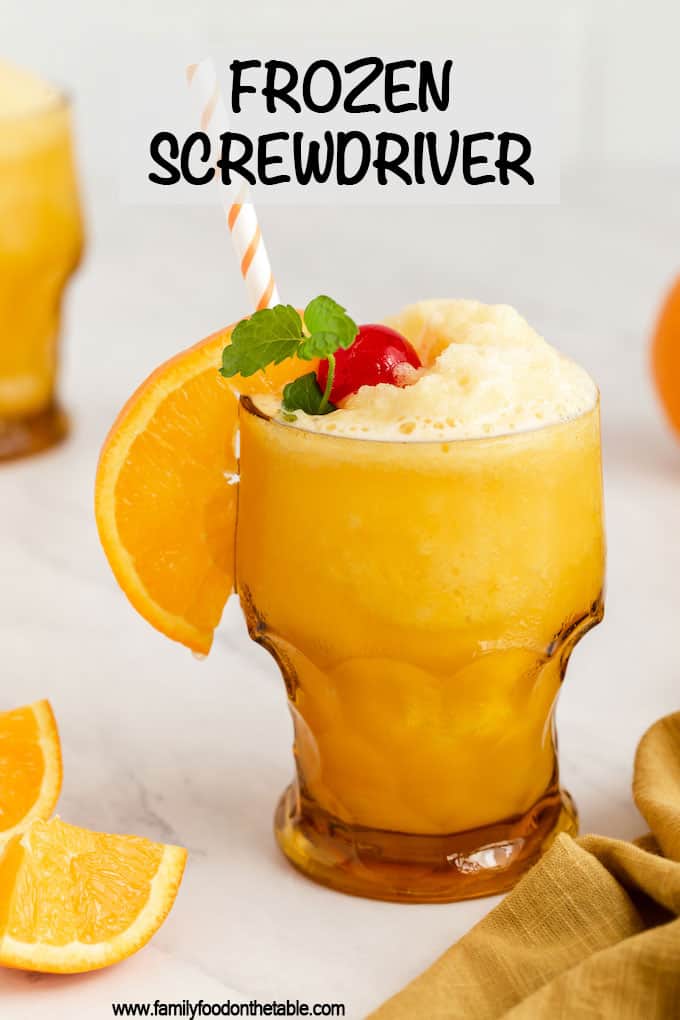 An amber glass with a slushy frozen screwdriver garnished with orange slice, cherry and a sprig of mint and a text overlay on the photo