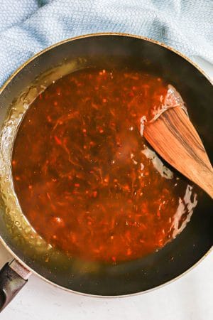 A sauce for healthy orange chicken being cooked in a large skillet with a spatula resting in it