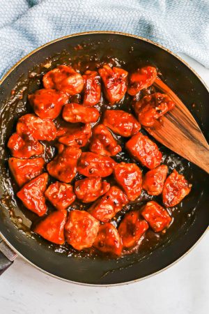 Crispy orange chicken pieces in a large dark skillet after being cooked and tossed in a sauce