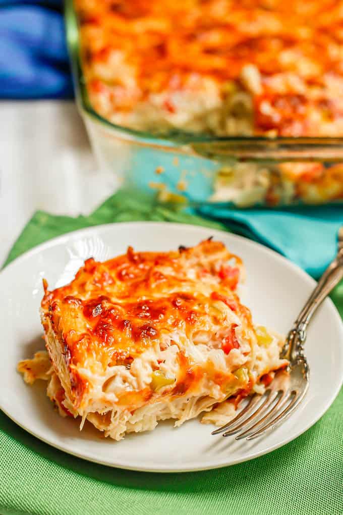 A serving of King Ranch chicken on a small white plate with a fork alongside and the rest of the casserole in the background