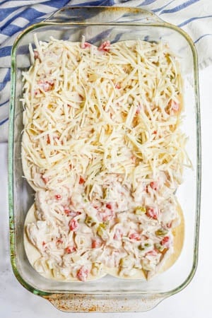 A King Ranch chicken casserole being assembled with cheese sprinkled on top in a large casserole dish